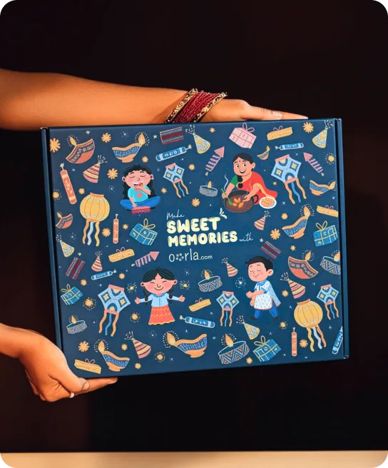 Two hands holding a navy Oorla gift box printed with Diwali illustrations and the line Make Sweet Memories.