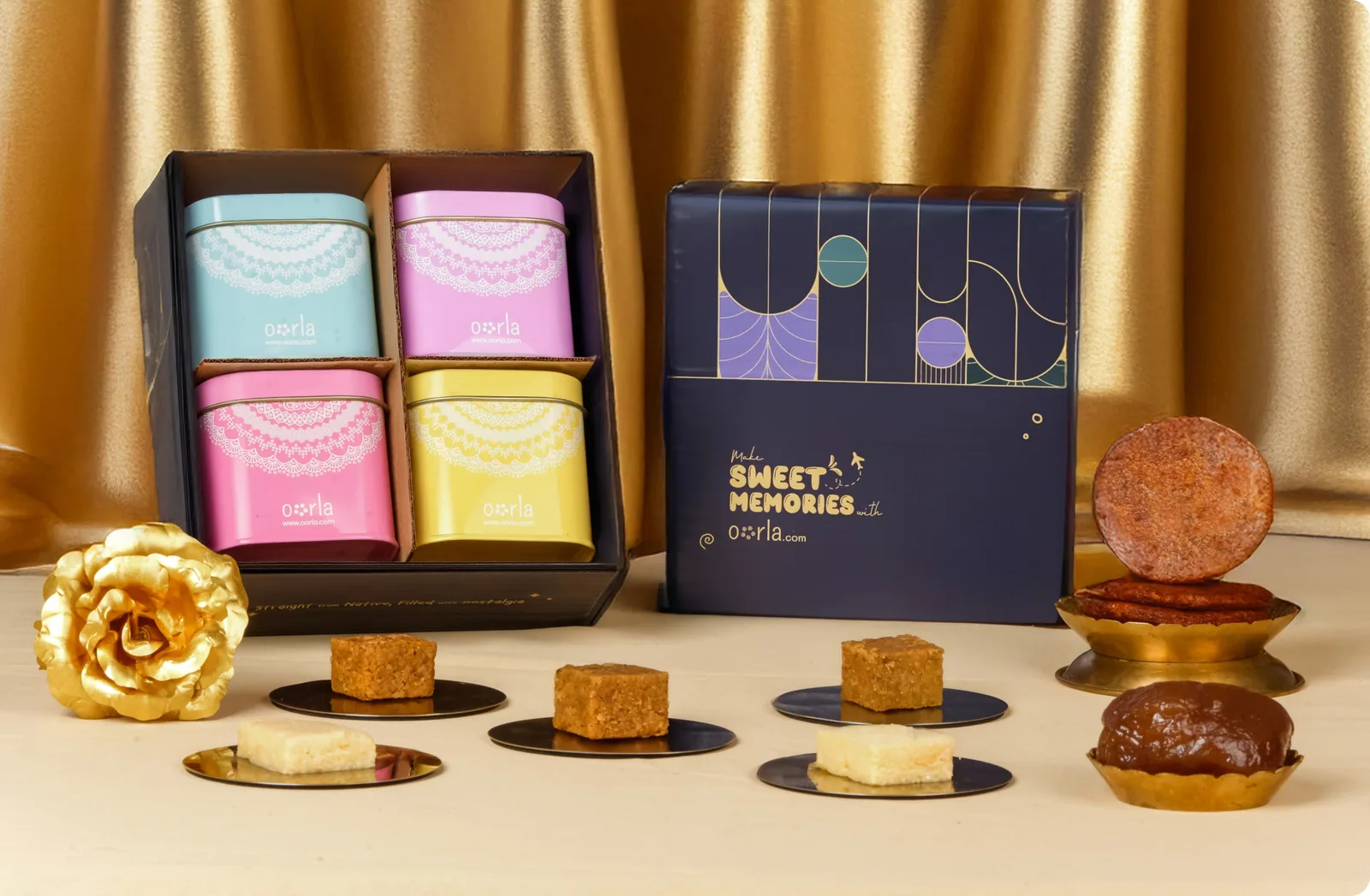 The Golden Bites hamper — four pastel sweet tins in an open keepsake box beside its navy printed lid, a gold rose and plated sweets, professionally staged