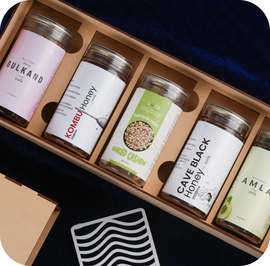 A wooden presentation box holding labelled glass jars of gulkand, Kombu honey, baked cashew, cave black honey and amla